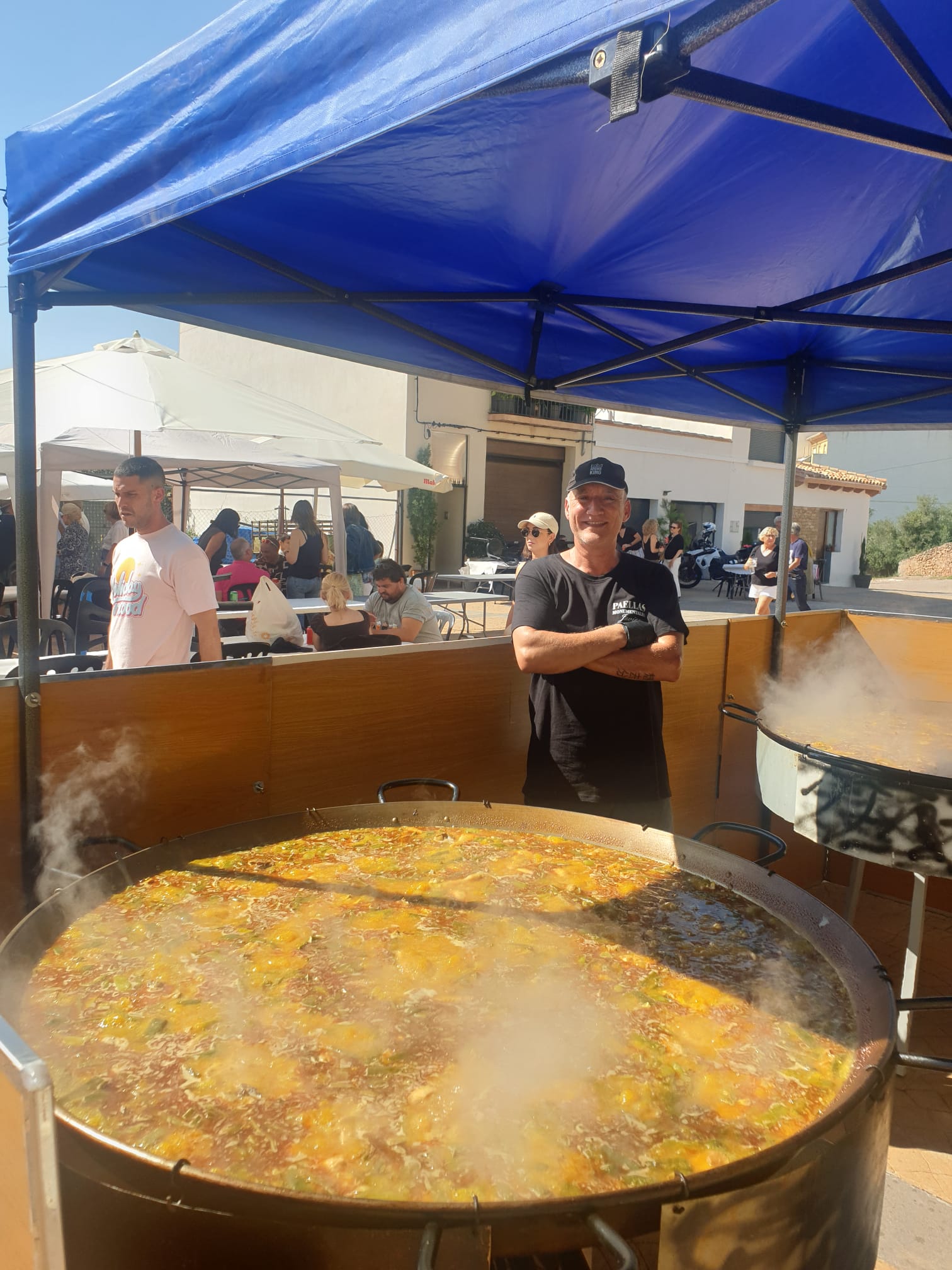 Chef de Paellas Monumentales Guiral junto a una paella gigante cocinándose al aire libre durante un evento comunitario.