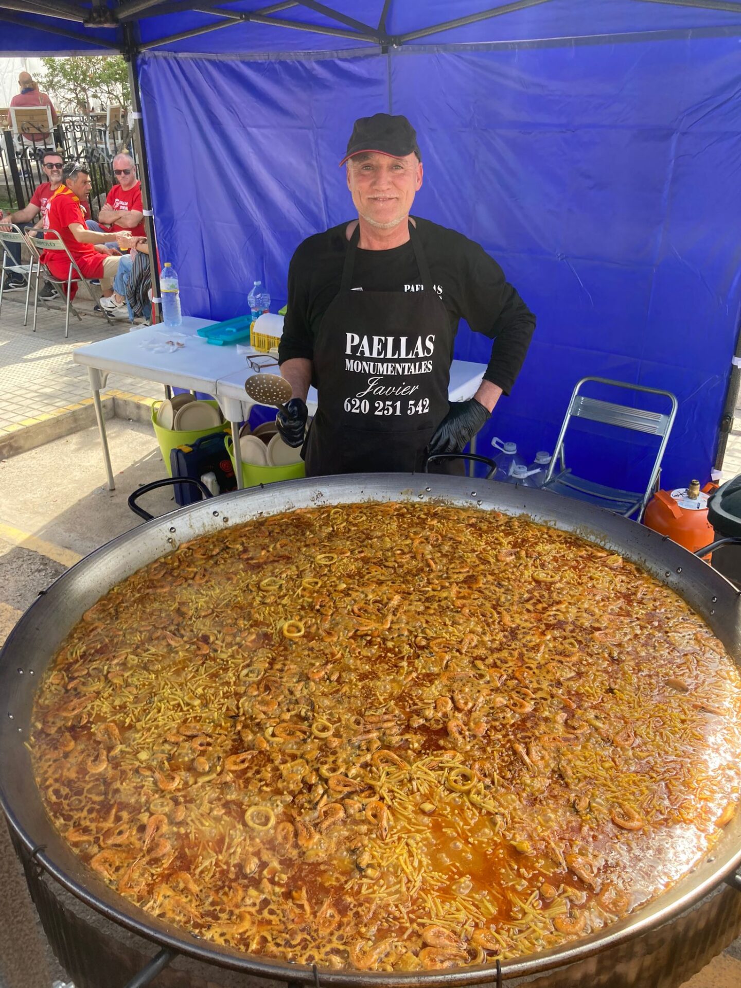 Chef Javier preparando una paella gigante de bacalao y sepia en un evento al aire libre, destacando su experiencia en paellas monumentales con ingredientes frescos y mariscos tradicionales.