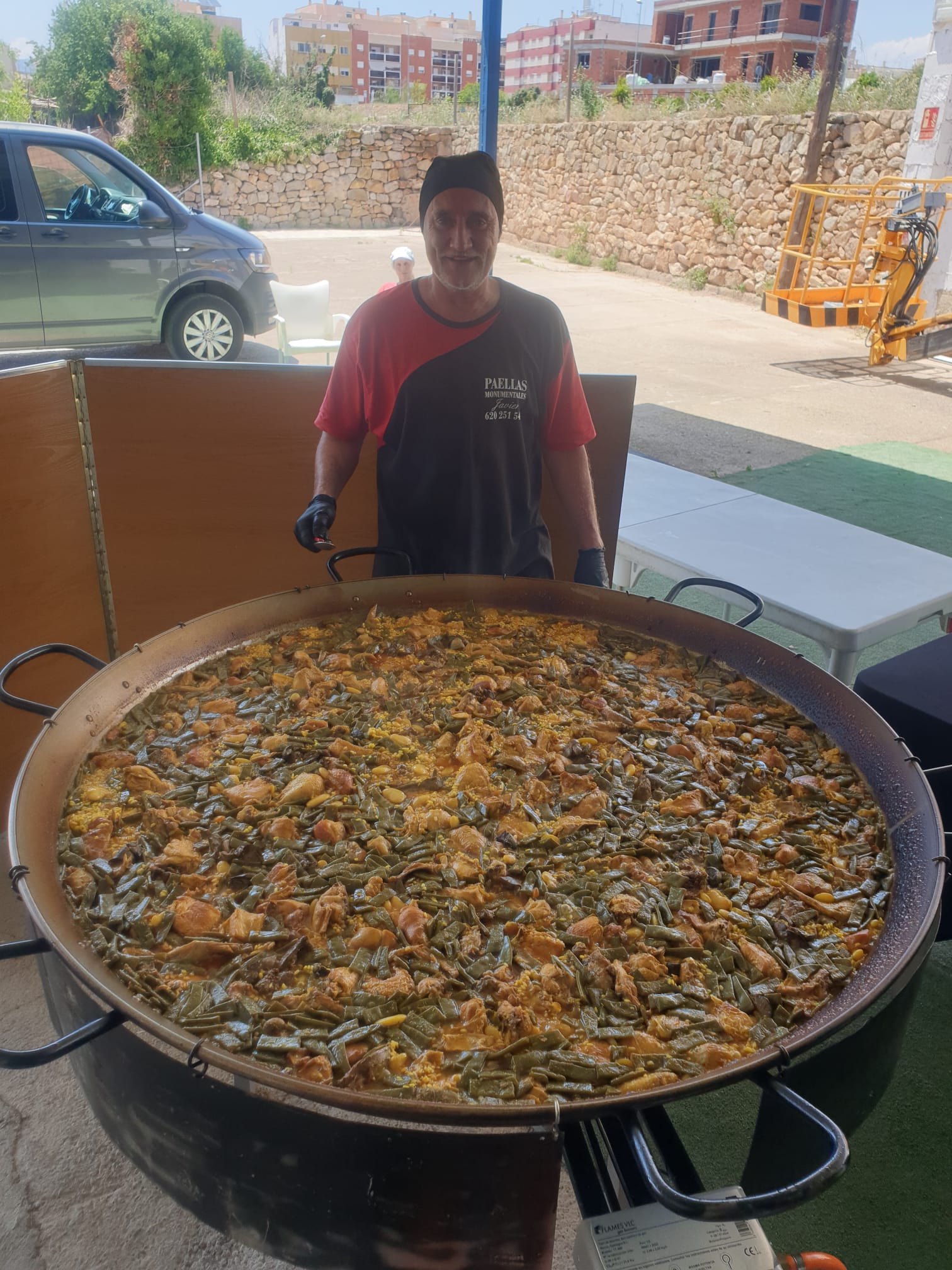 Chef de Paellas Monumentales Guiral junto a una paella valenciana gigante con pollo, conejo y judías verdes, perfecta para eventos y celebraciones.