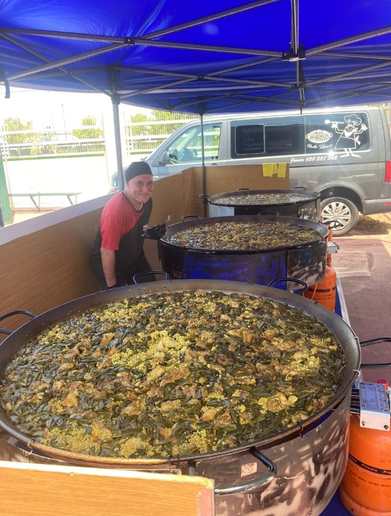 Cocinero junto a paelleras gigantes llenas de paella valenciana tradicional, cocinadas al aire libre como parte de un evento organizado por Guiral.