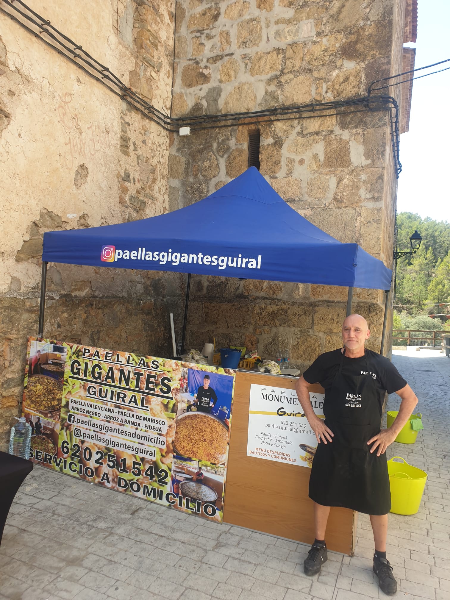 Stand de Paellas Gigantes Guiral con chef y cartel promocional, especializado en paellas valencianas y fideuás para eventos y servicio a domicilio.